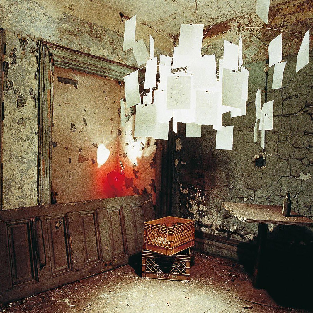A Clérachic paper pendant hangs in a weathered, peeling room, its white paper notes glowing against the old walls.