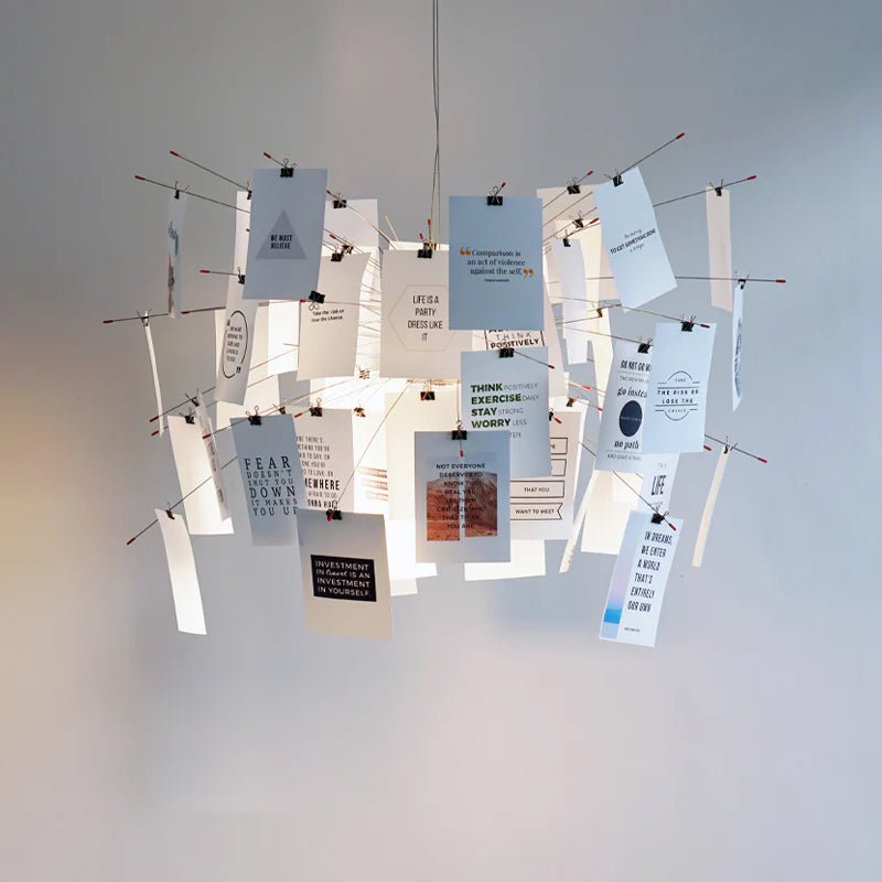Cards printed with short quotes in black and blue hang from the arms of this Clérachic pendant against a plain pale wall.
