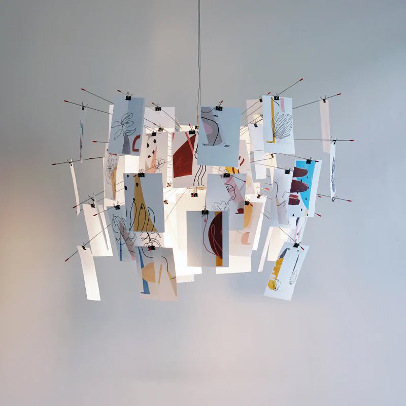 This Clérachic paper pendant carries cards with abstract line drawings in rust, blue and tan against a plain grey-blue wall.