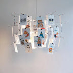 A Clérachic pendant hung with cards of cartoon animals, from bears to owls, on red-tipped wire arms, in front of a pale wall.