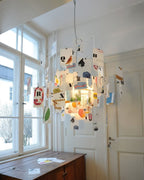 Lit warmly beside tall windows, a Clérachic pendant with printed letter cards and wire arms hangs over a wooden chest.