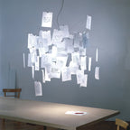A Clérachic paper pendant over a table in a blue-grey room, with handwritten notes lit softly from inside the frame.