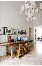 High in a white hallway above a long wooden desk, a Clérachic paper pendant fills the top of the frame with notes.