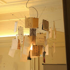 A warm amber glow lights the notes on this Clérachic pendant, with thin wire arms spread against ornate ceiling plasterwork.