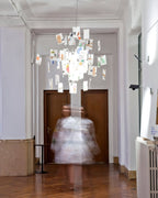 At the end of a long hall, a Clérachic paper pendant with colourful printed cards hangs above a blurred figure.