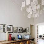 Above a wooden desk with a lamp and a framed print gallery, this Clérachic paper pendant spills notes across the ceiling.
