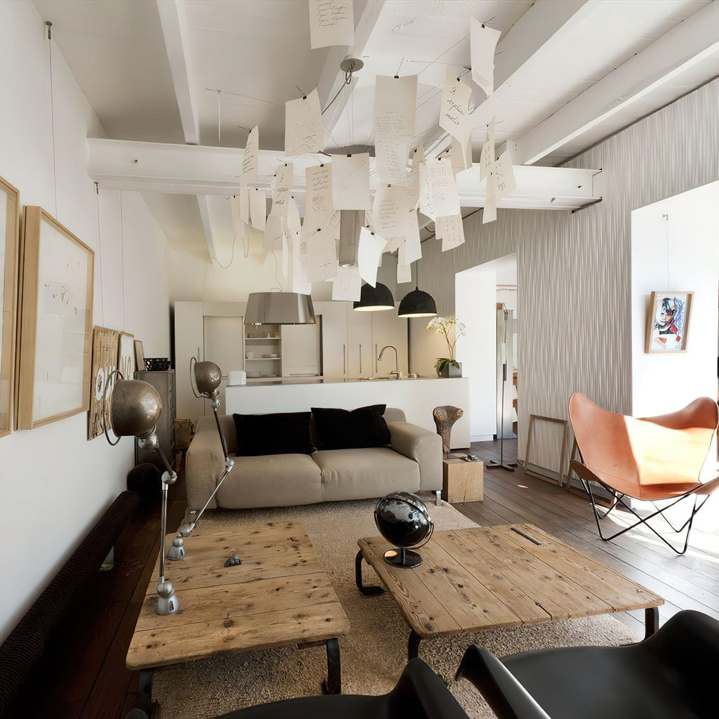 Over a rustic table and a leather butterfly chair, a Clérachic paper pendant hangs in a loft living room with white beams.