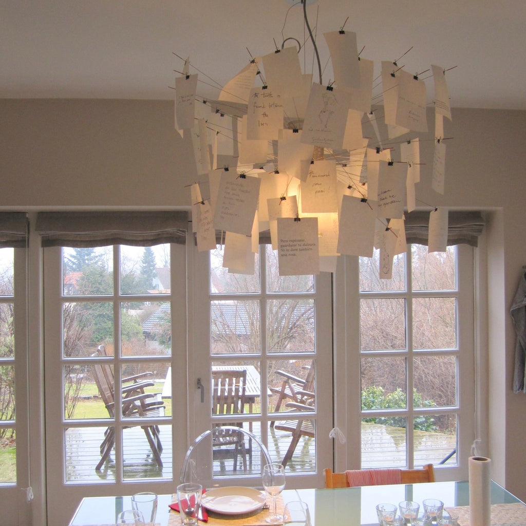 In front of tall glazed doors, a Clérachic paper pendant is full of handwritten notes, glowing warm above a laid table.