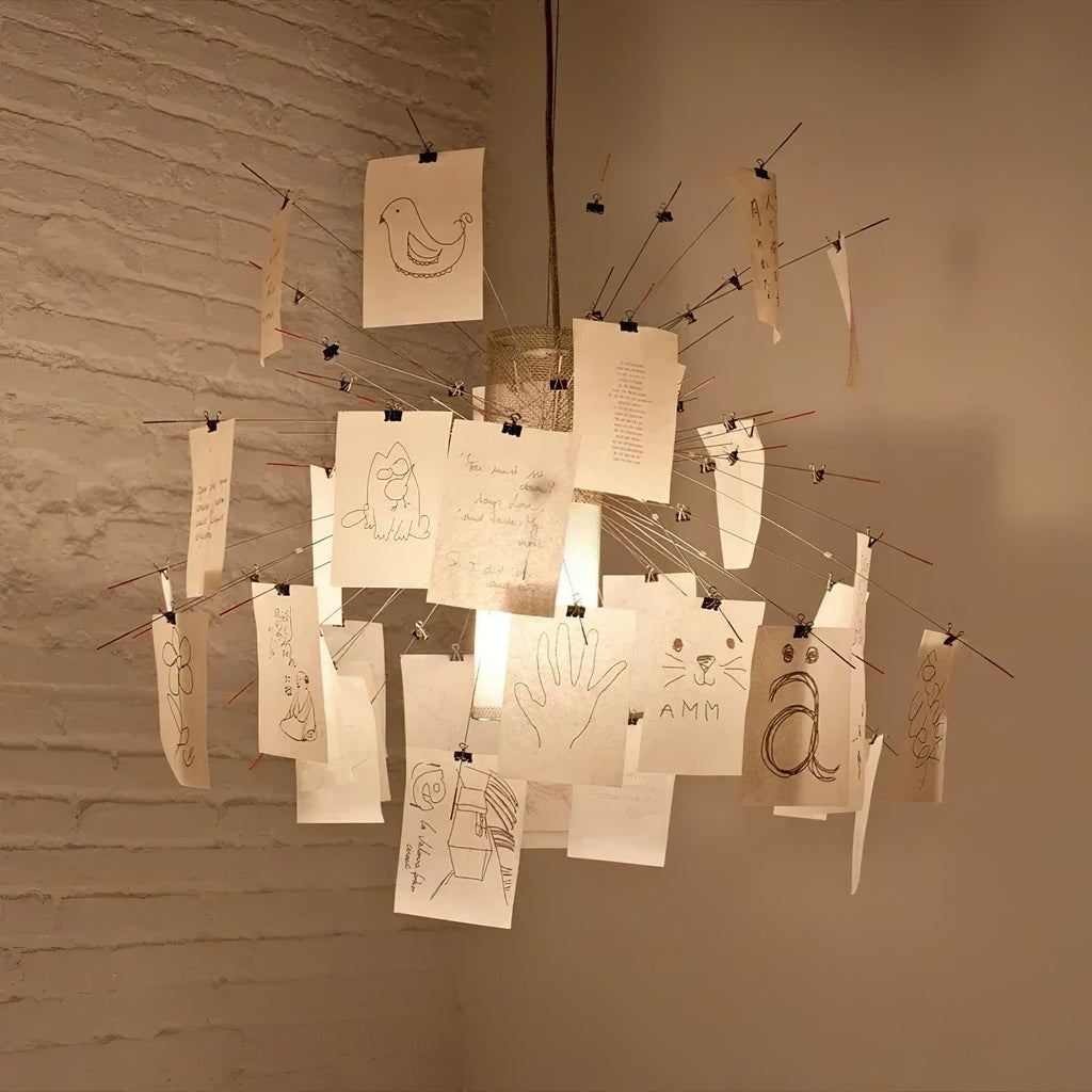 Sketches of birds, hands and faces are drawn on the cards of this Clérachic pendant, lit warm against a white-painted brick wall.