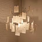 Sketches of birds, hands and faces are drawn on the cards of this Clérachic pendant, lit warm against a white-painted brick wall.
