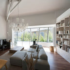 In a bright living room with a grey sectional sofa, a Clérachic paper pendant hangs in the upper left of the frame.