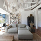 Above a grey sofa and shelves of books, a Clérachic paper pendant stretches across the ceiling beams of a white loft.