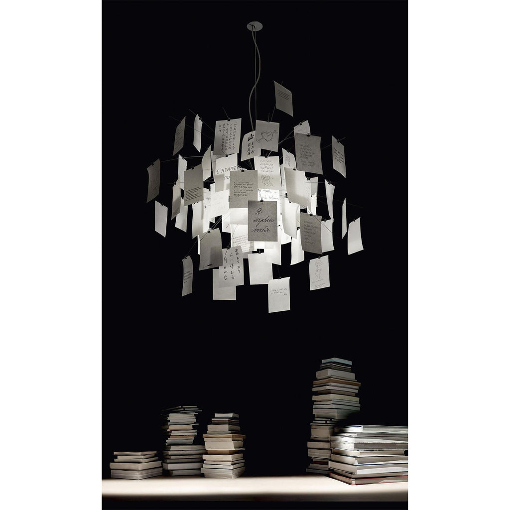 On a black background above stacks of books, a Clérachic paper pendant glows with handwritten notes.