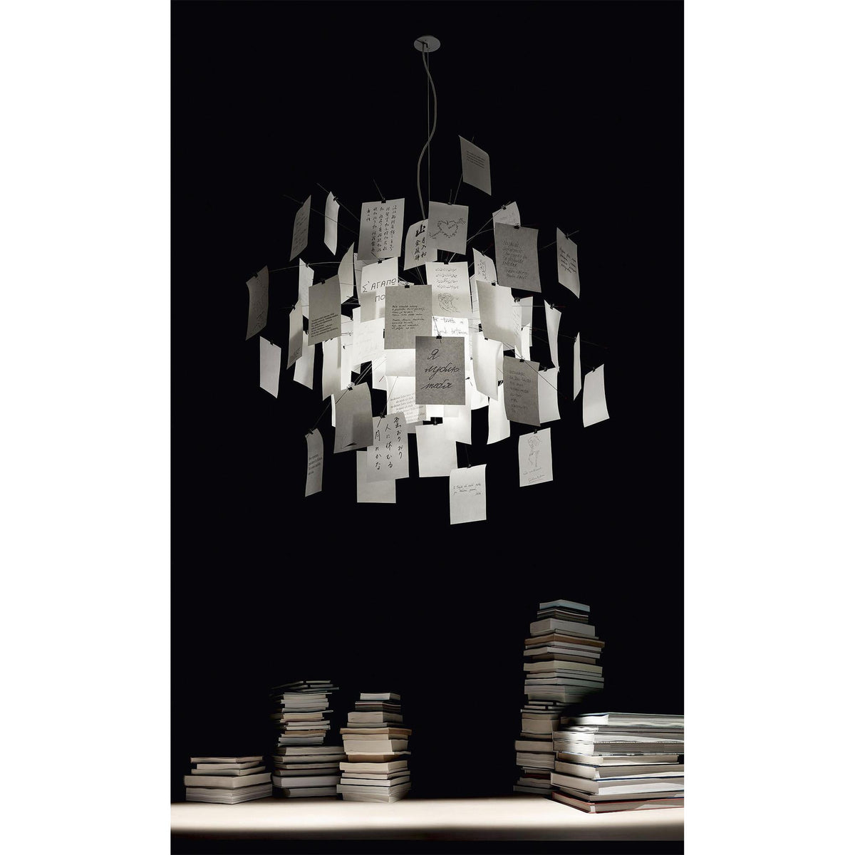 On a black background above stacks of books, a Clérachic paper pendant glows with handwritten notes.