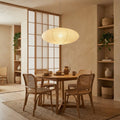 Clérachic wide paper pendant light glowing above a round wooden dining table with cane-backed chairs and a shoji screen behind.