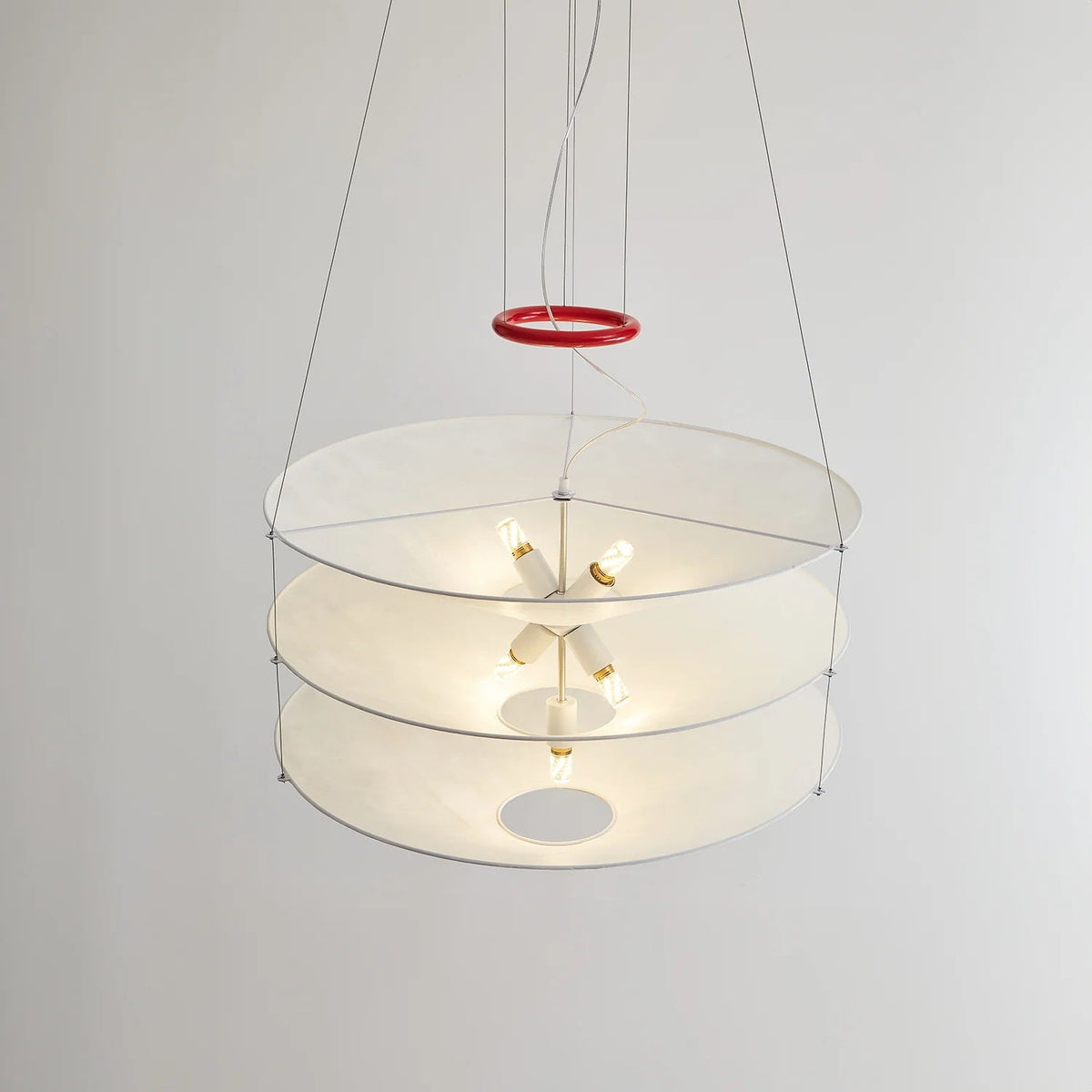 Seen from the side against a plain wall, the three paper tiers of this Clérachic pendant show small bulbs lit inside, with a red ring on the cables.
