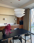 A Clérachic three-tier white pendant hangs over a black dining table in a kitchen-diner with a tall window and wood cabinets.