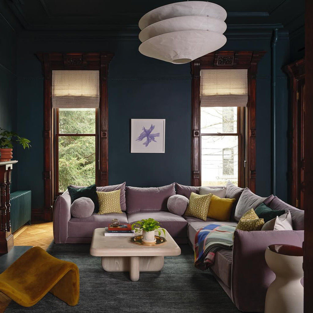 A Clérachic pendant of three stacked white paper tiers hangs in a deep teal room above a lilac sofa and a pale coffee table.