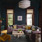 A Clérachic pendant of three stacked white paper tiers hangs in a deep teal room above a lilac sofa and a pale coffee table.