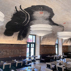 A Clérachic tiered paper pendant hangs in a vaulted brick restaurant with a large painted figure on the ceiling above the tables.