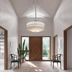A Clérachic three-tier white pendant hangs in a high-ceilinged entrance hall with a wooden front door, two chairs and a tall cactus.