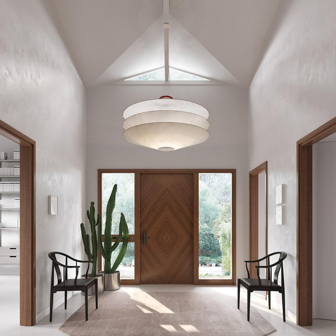 A Clérachic three-tier white pendant hangs in a high-ceilinged entrance hall with a wooden front door, two chairs and a tall cactus.