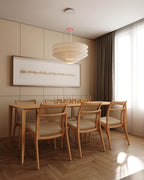 A Clérachic tiered paper pendant hangs above a long light wood dining table with six chairs, in front of a framed artwork.