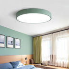A sage-green Clérachic flush mount ceiling light sits flush above a green bedroom lined with framed art.