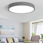 A warm-grey Clérachic flush mount ceiling light is shown at an angle, lighting a cozy living room seating area.