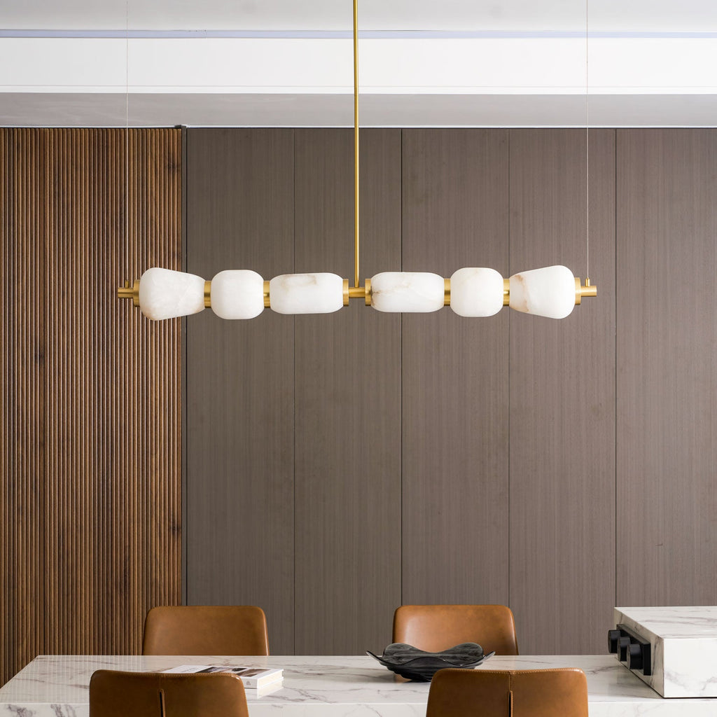 Close, straight-on view of the six-pebble Clérachic chandelier in gold, hung against dark fluted wood panelling above a marble table.