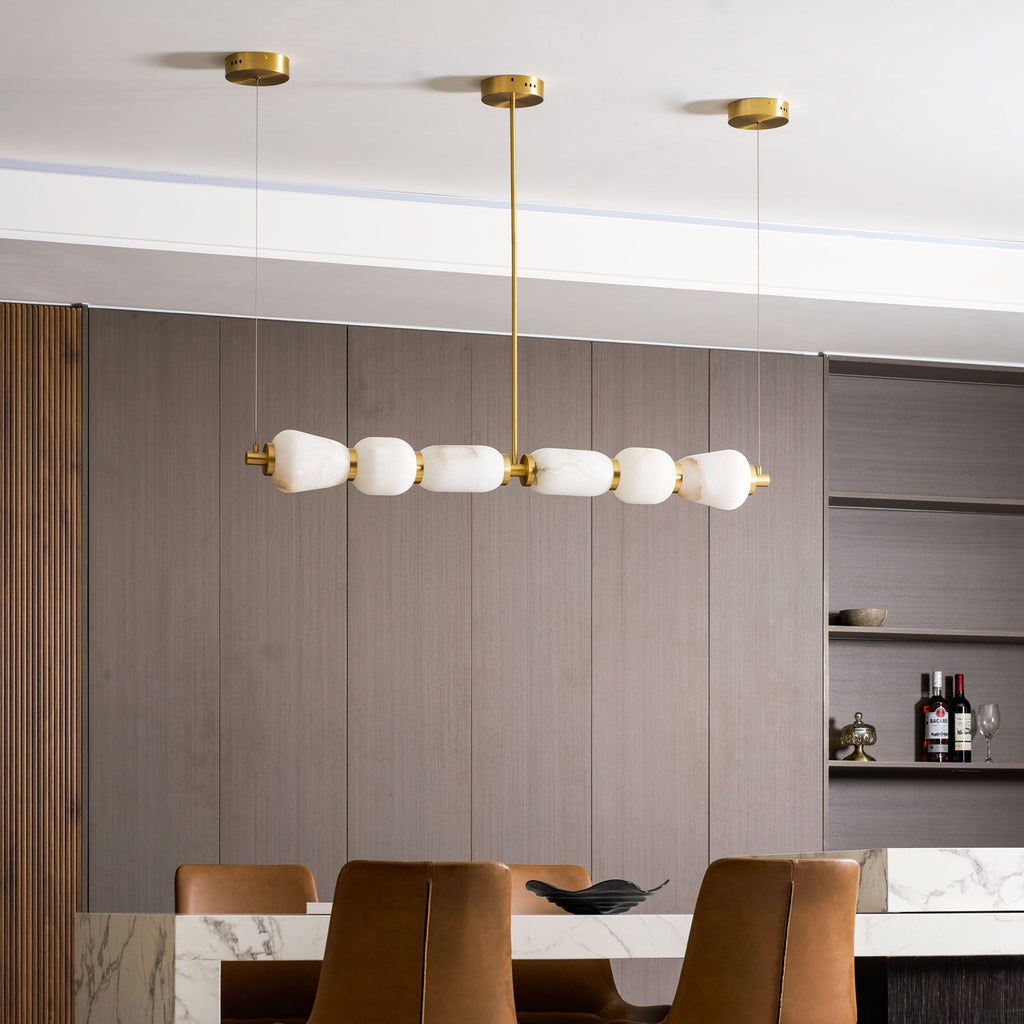 Side-on view of this Clérachic pebble chandelier and its gold central rod, unlit, with shelving and a marble table beneath.