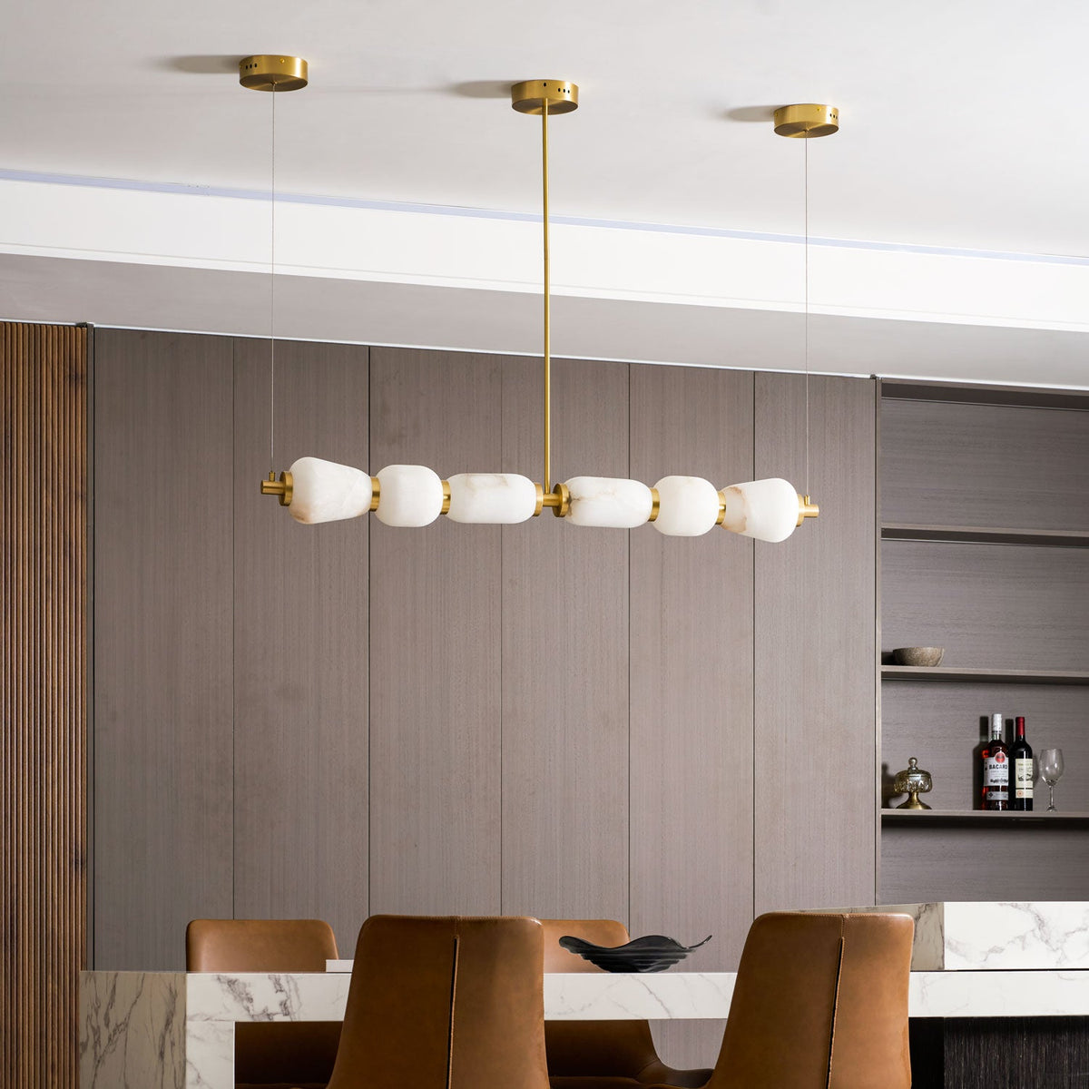 Side-on view of this Clérachic pebble chandelier and its gold central rod, unlit, with shelving and a marble table beneath.