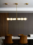 Lit warm and glowing, the pebbles of this Clérachic chandelier hang below three gold canopies over a marble table and leather chairs.