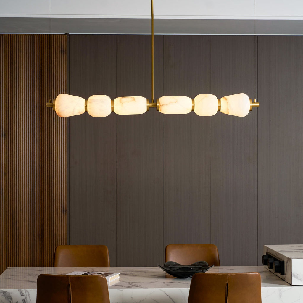Close, lit view of this Clérachic chandelier's six alabaster pebbles joined by gold bands, against dark panelled wall and a marble table.