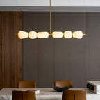 Close, lit view of this Clérachic chandelier's six alabaster pebbles joined by gold bands, against dark panelled wall and a marble table.