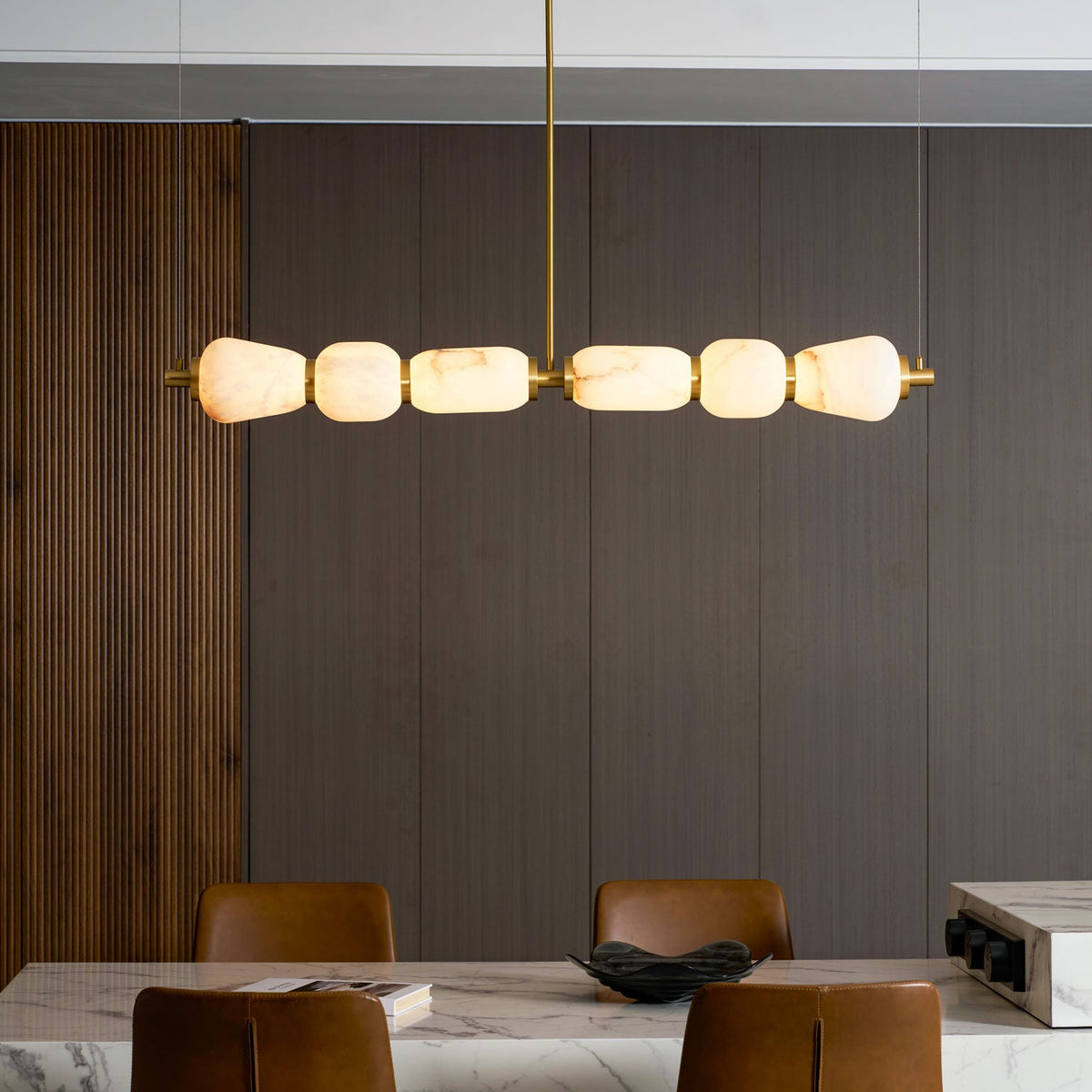 Close, lit view of this Clérachic chandelier's six alabaster pebbles joined by gold bands, against dark panelled wall and a marble table.