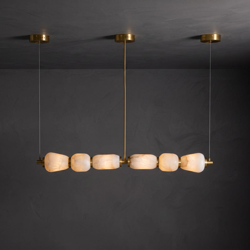 Lit six-pebble Clérachic chandelier with gold fittings hanging against a dark plaster wall, the alabaster glowing amber.