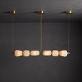 Lit six-pebble Clérachic chandelier with gold fittings hanging against a dark plaster wall, the alabaster glowing amber.