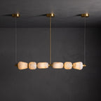 Lit six-pebble Clérachic chandelier with gold fittings hanging against a dark plaster wall, the alabaster glowing amber.