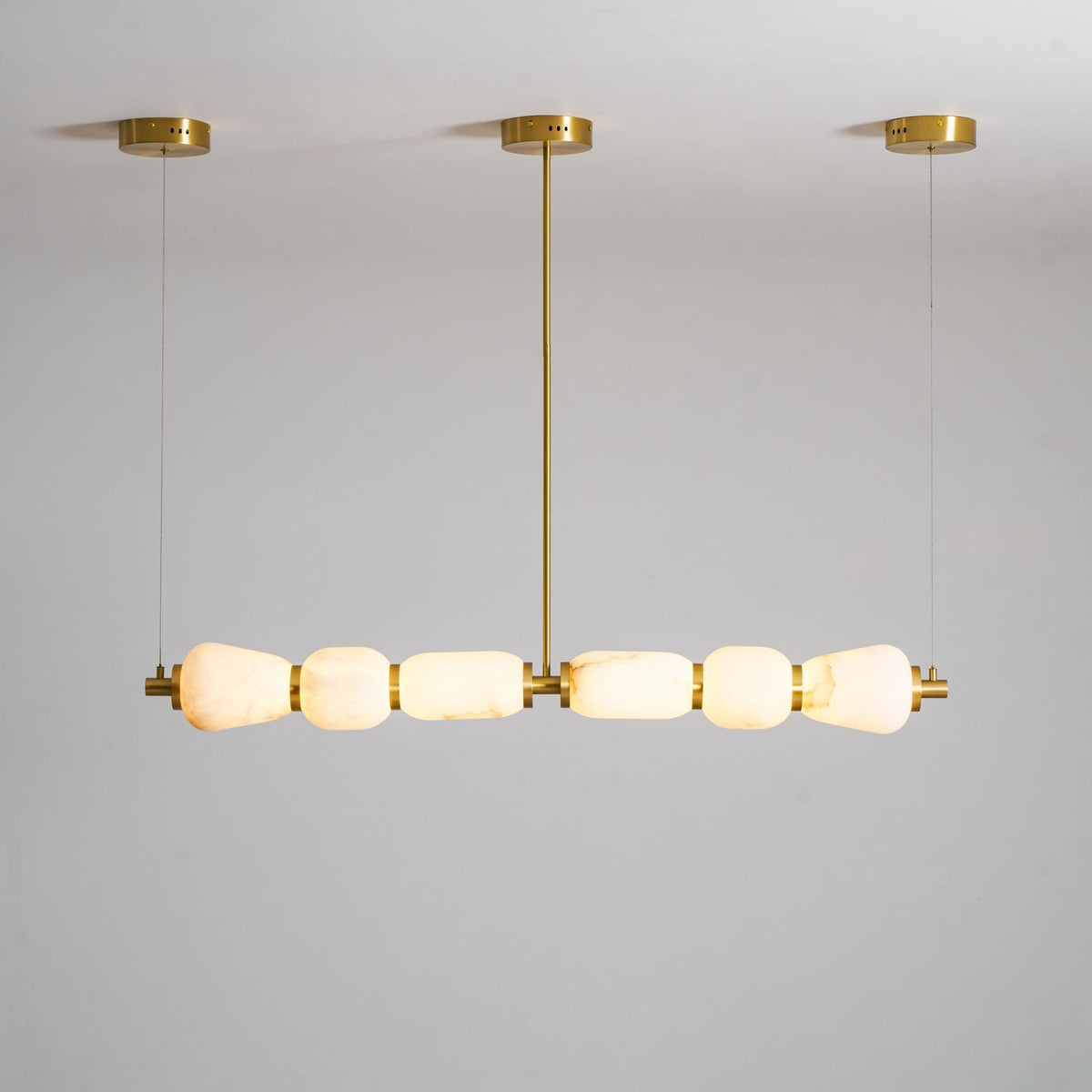 Gold-fitted Clérachic chandelier with six lit alabaster pebbles, shown from a low angle against a pale grey ceiling and wall.