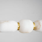 Close view of creamy white alabaster on this Clérachic chandelier, a gold band joining two pebbles against a soft grey backdrop.