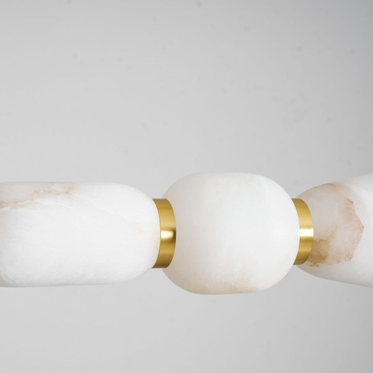 Close view of creamy white alabaster on this Clérachic chandelier, a gold band joining two pebbles against a soft grey backdrop.