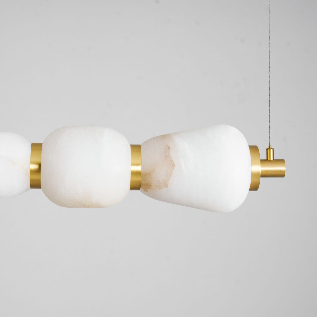 Close view of the end pebble of this Clérachic chandelier, with white veining in the alabaster and a gold band at the hanging point.