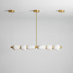 Unlit Clérachic linear chandelier in gold and white, with six alabaster pebbles under three gold canopies against a pale grey wall.