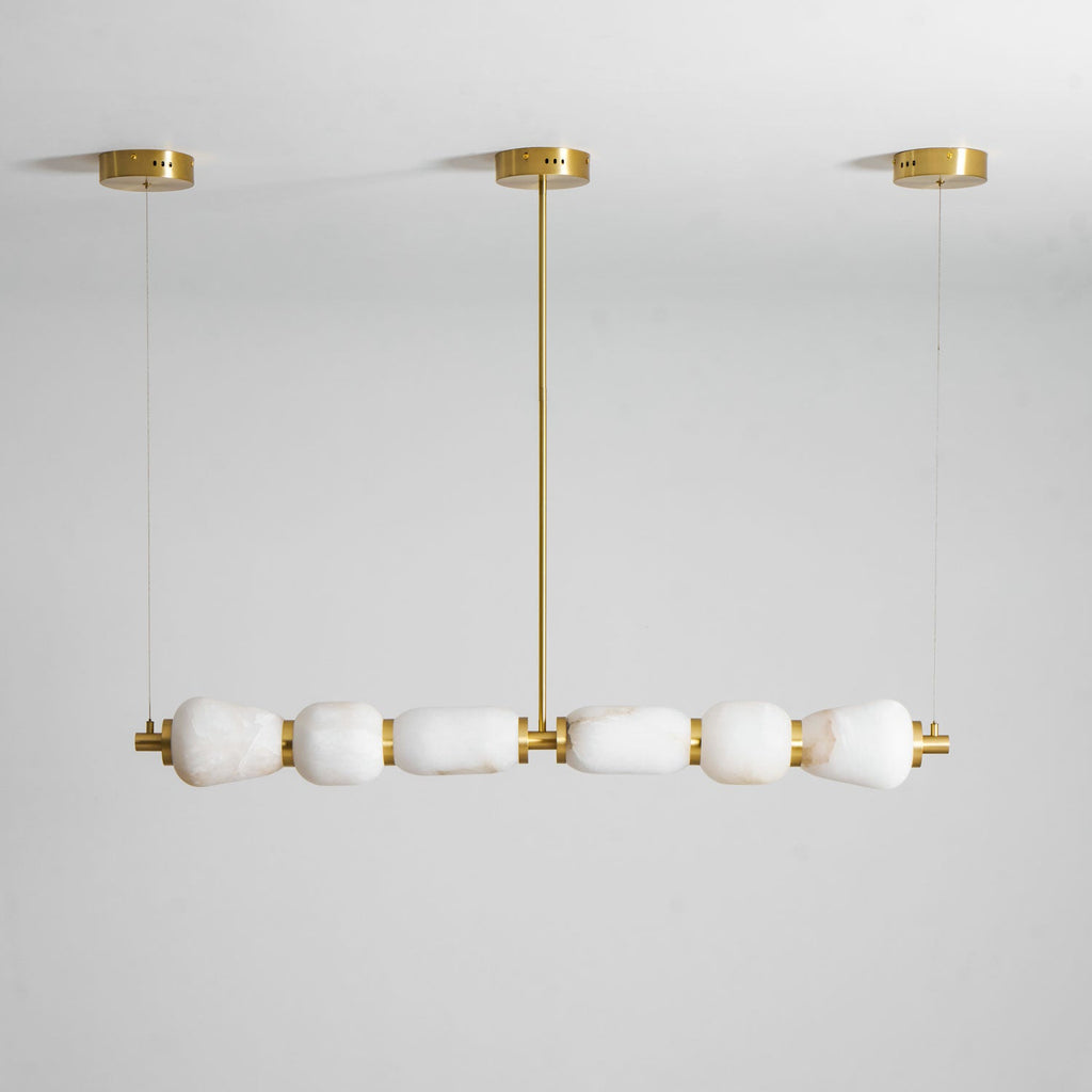 Another view of this Clérachic pebble chandelier unlit, its gold rod and cords reaching up to the canopies on a soft grey wall.