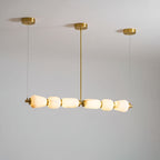 From a lower angle, the lit pebbles of this Clérachic linear chandelier glow warm white under its gold ceiling canopies.
