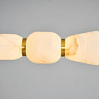 Close view of a lit alabaster pebble on this Clérachic chandelier, glowing from within beside a gold ring on a grey backdrop.