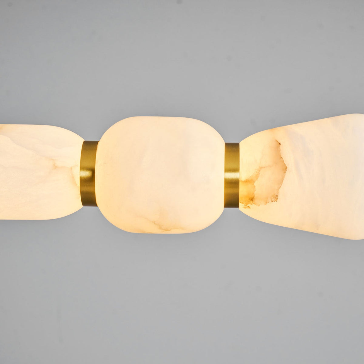 Close view of a lit alabaster pebble on this Clérachic chandelier, glowing from within beside a gold ring on a grey backdrop.