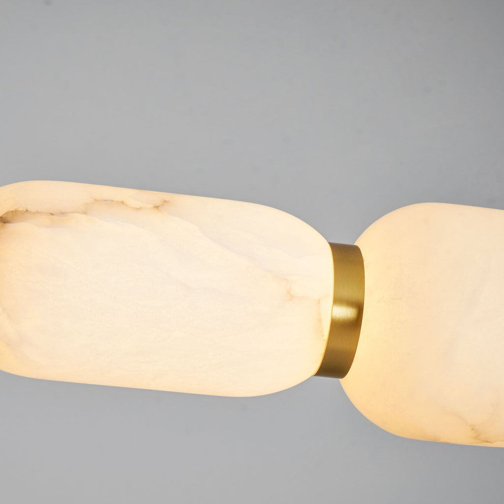 Close view of alabaster veining in a long pebble of this Clérachic chandelier, glowing softly beside a gold band against grey.