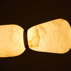 Close view of two lit pebbles on this Clérachic chandelier, the alabaster veining glowing golden against a dark background.